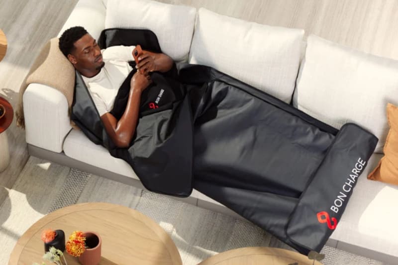 Man using BonCharge infrared sauna blanket on white couch with phone in hand