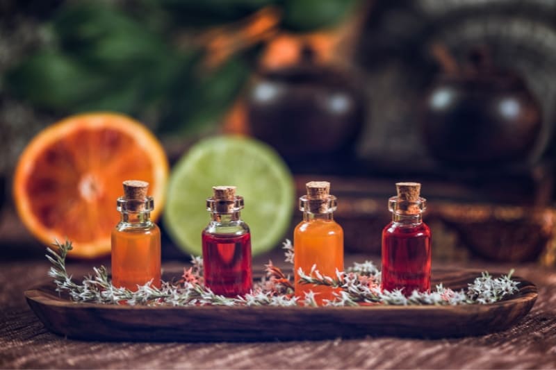 4 bottle filled with citrus essential oil in red and orange color on a wooden tray with freshly cut lemon and orange in the background