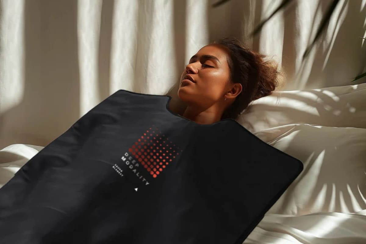 Close-up of a woman using Deep Modality infrared sauna blanket with red dot pattern design logo