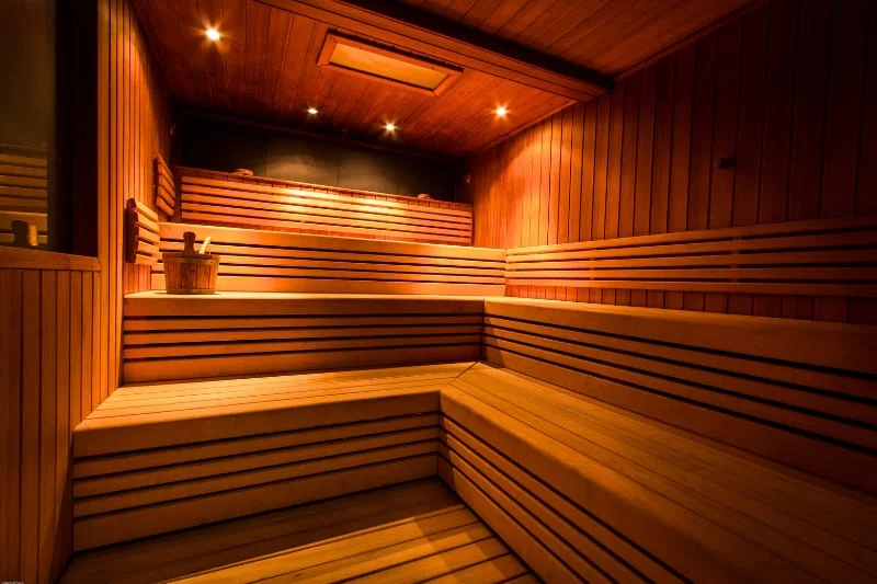 Traditional Finnish wooden sauna interior featuring tiered benches, cedar paneling, ambient lighting, and modern heating system in warm orange glow, showcasing classic Nordic spa design