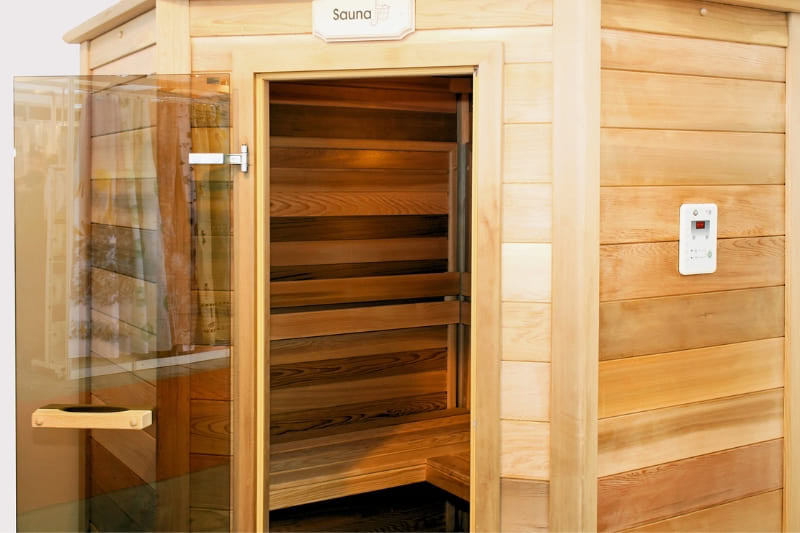 Professional gym sauna entrance with glass door, digital temperature controls, and natural wood construction