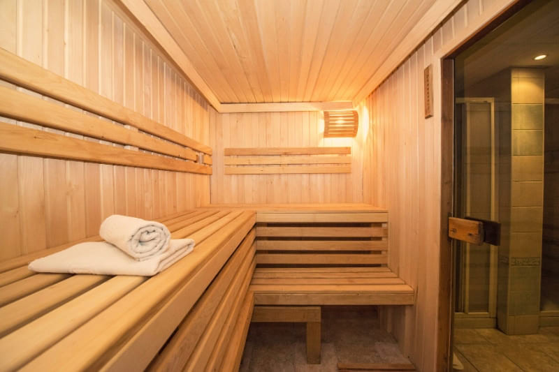 Clean gym sauna interior with white towels, multi-level wooden benches, and ventilation system for optimal wellness experience