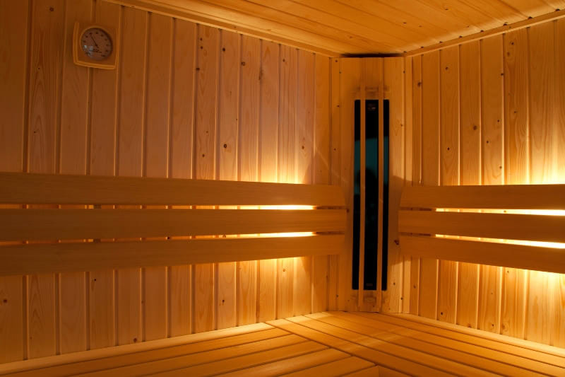 Infrared sauna room with ambient lighting, wall-mounted thermometer, and ergonomic wooden bench design