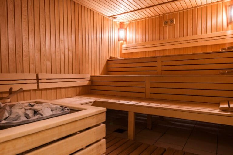 Modern gym sauna interior with tiered wooden benches and traditional hot stones, featuring warm lighting and cedar wood paneling