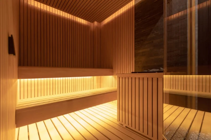 Interior view of high-end indoor sauna with ambient LED lighting, wooden benches, and vertical slat wall design