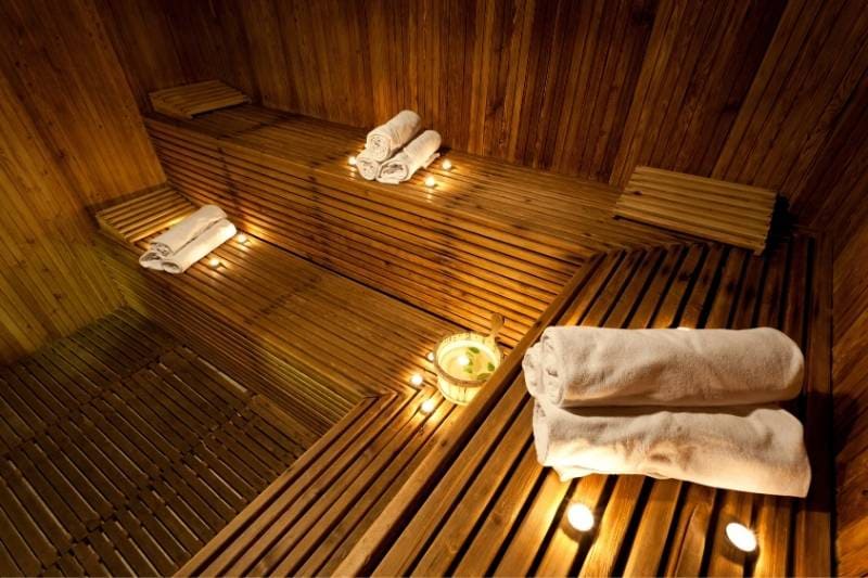 Luxurious wellness sauna featuring soft candlelight, plush white rolled towels, and premium wooden architecture