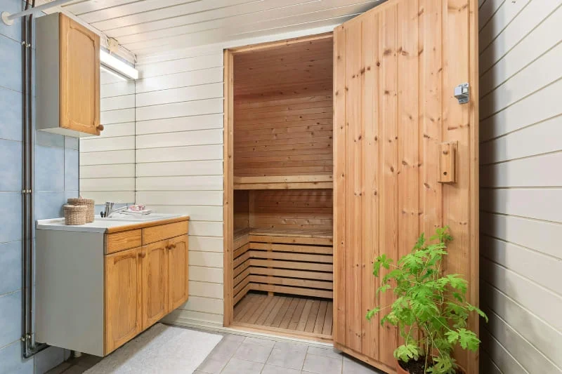 Custom indoor sauna installation in bathroom with pine wood construction, glass door, and modern vanity setup