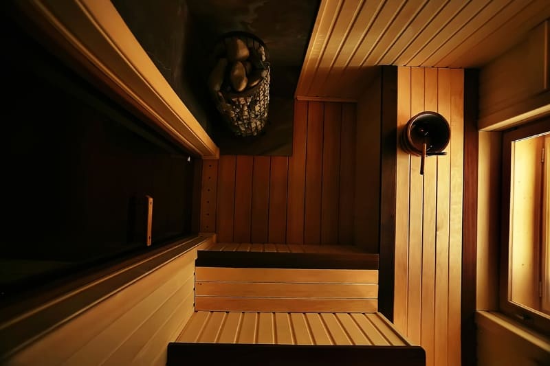 Top view of an interior of a wooden sauna with tiered benches, a light fixture, and a dark ambiance.