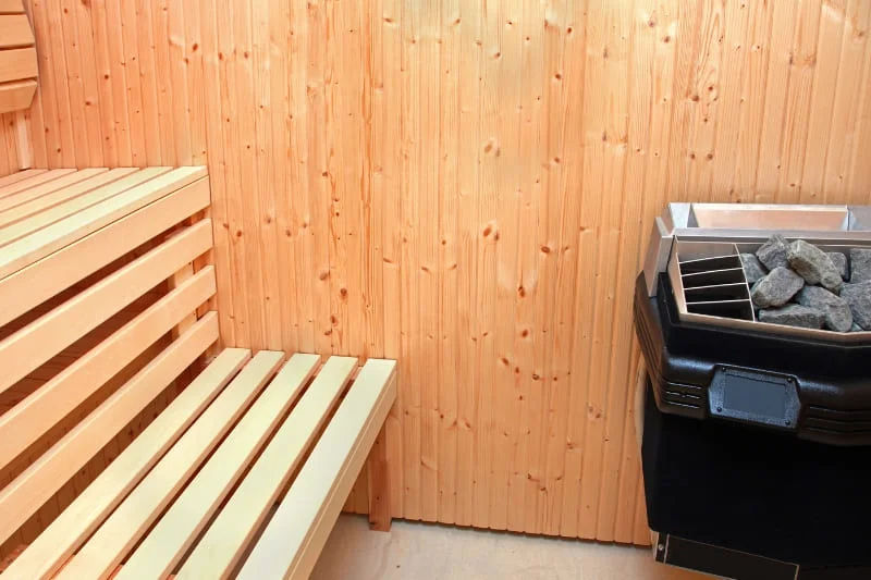 Traditional Finnish-style indoor sauna interior showing wooden bench seating and electric sauna heater with stones