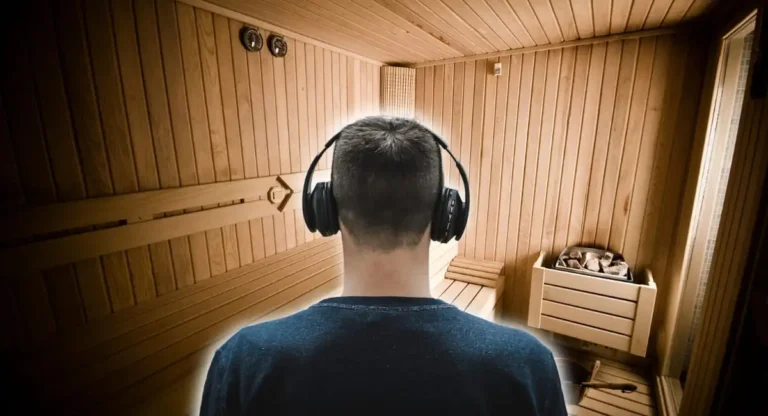 A man wearing over-ear wireless headphones in a traditional wooden sauna with temperature gauges, demonstrating heat-resistant audio equipment for relaxation during high-temperature sauna sessions