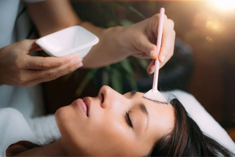 Skincare specialist applying chemical peel with retinol serum using an applicator brush during professional facial treatment