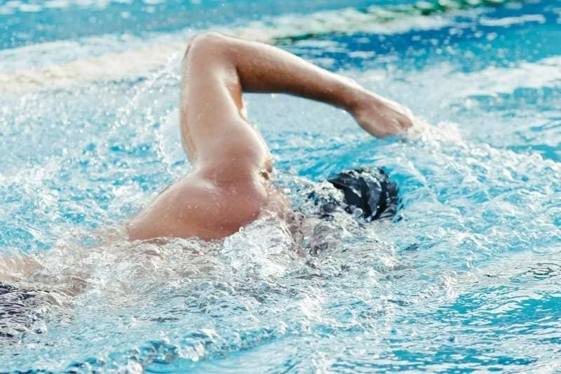 Swimmer performing freestyle stroke in clear blue swimming pool water, arm extended during mid-stroke.