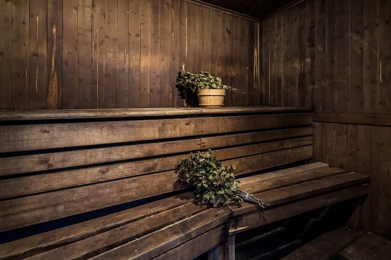 Interior of a traditional Finnish sauna with wooden benches and birch whisks, showing the authentic sauna environment for cardiovascular health benefits.