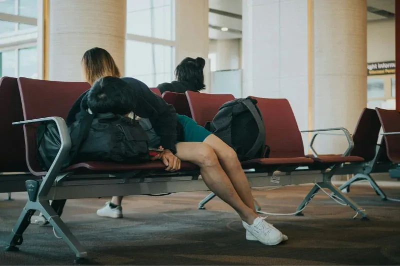 Travelers sleeping on airport seats between flights, demonstrating how long-distance travel disrupts normal sleep patterns.