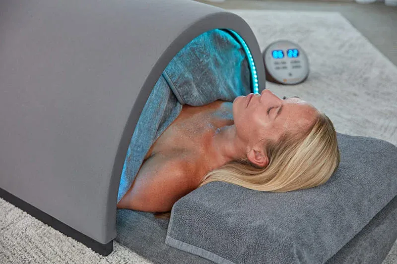 A woman enjoying the Sunlighten Solo sauna featuring blue chromotherapy lighting for enhanced relaxation benefits.