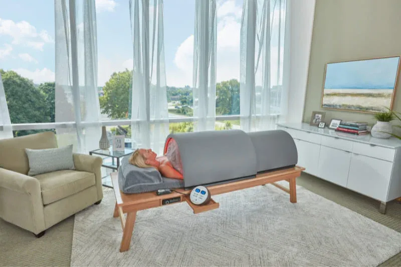 Sunlighten Solo infrared sauna fully assembled on wooden stand in modern living room with person using it.