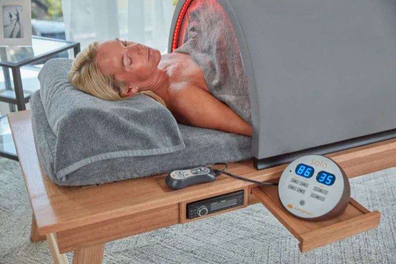 Sunlighten Solo infrared sauna with red light therapy illuminating the interior as user relaxes on comfortable pillow.