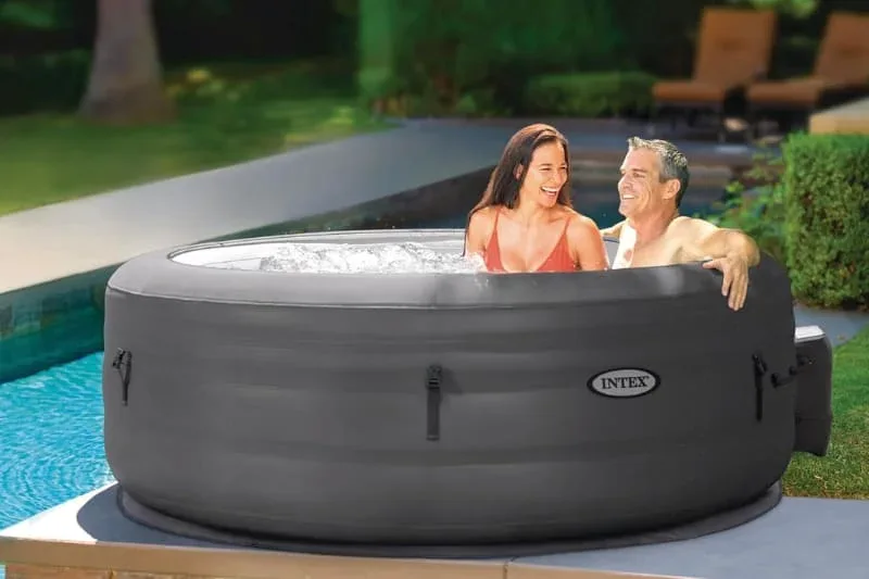 Intex inflatable hot tub in dark gray with couple relaxing by swimming pool, portable spa with bubble jets in luxury backyard setting with pool deck