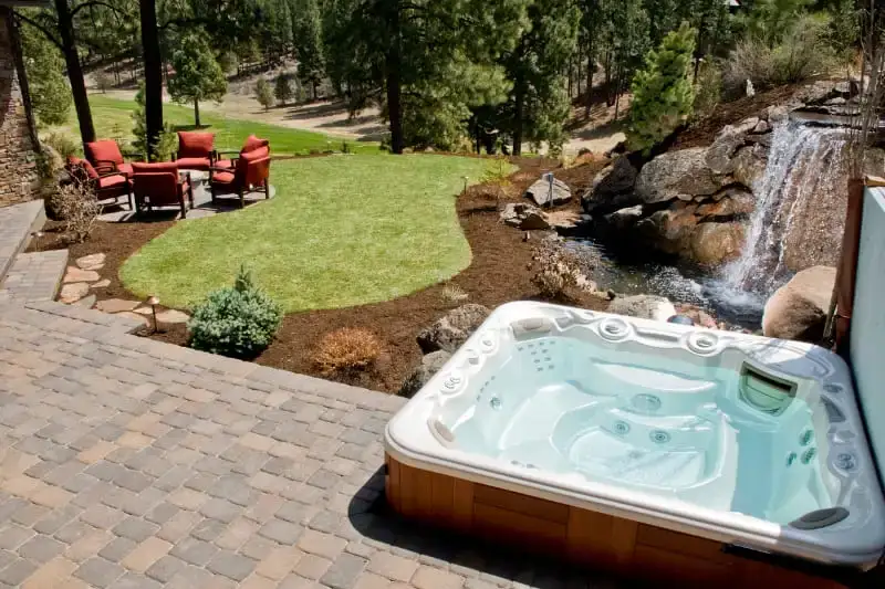 Luxury hot tub spa in landscaped backyard with natural stone waterfall and patio seating area