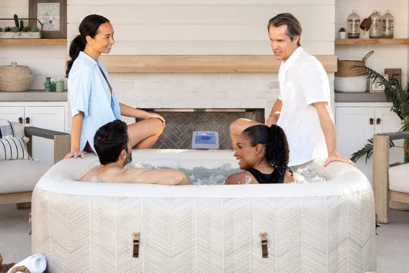Four friends relaxing in a white inflatable hot tub with bubble jets in modern living room setting with kitchen background