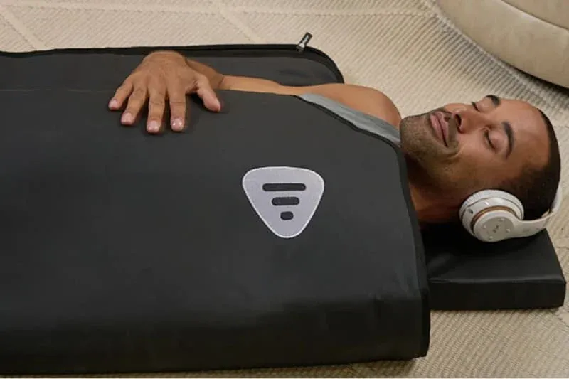 Man enjoying LifePro RejuvaWrap sauna blanket therapy session with headphones for relaxation