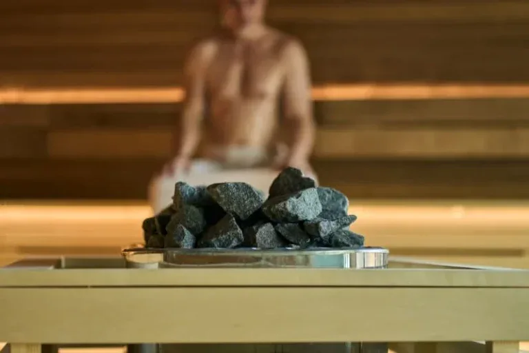 Sauna stones displayed on bench with person relaxing in background demonstrating proper sauna stone selection for authentic Finnish sauna experience