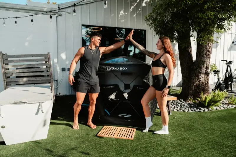 Happy couple high-fiving after steam therapy session with SaunaBox GO two-person portable sauna in background