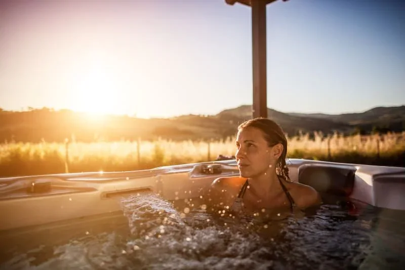 Woman experiencing hot tub benefits during golden hour sunset session for wellness and relaxation