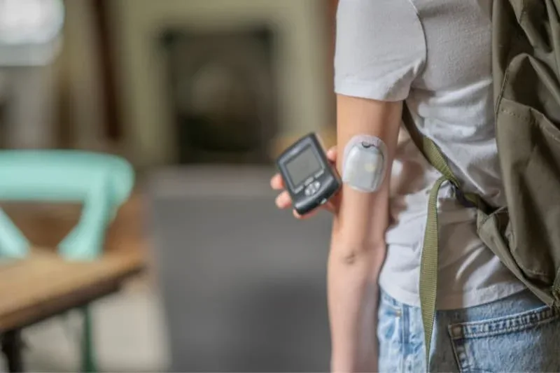Person wearing continuous glucose monitor on arm while holding blood sugar reader device for diabetic scanning