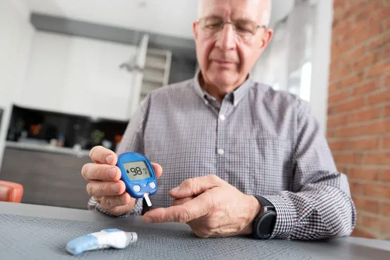 Elderly man holding blood glucose meter showing 98 mg/dL reading for diabetes management