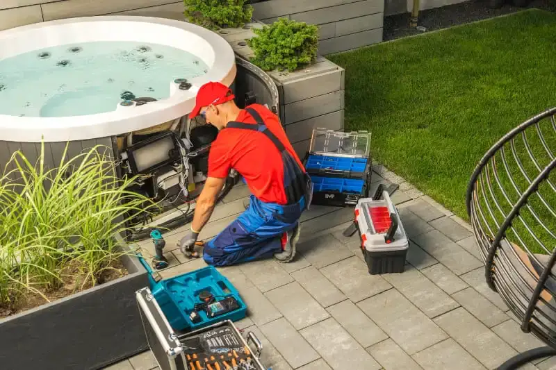 Professional spa technician repairing hot tub equipment and plumbing underneath spa unit