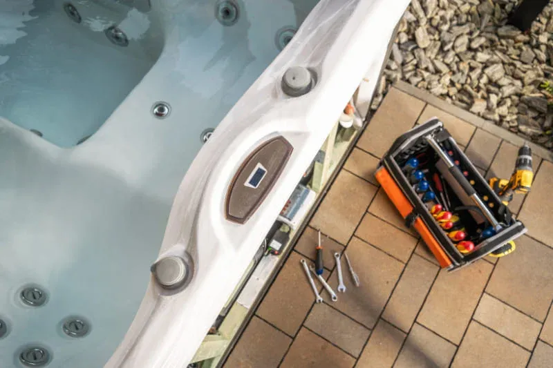 Professional technician with toolbox working on hot tub electrical components and plumbing systems for repair or removal preparation