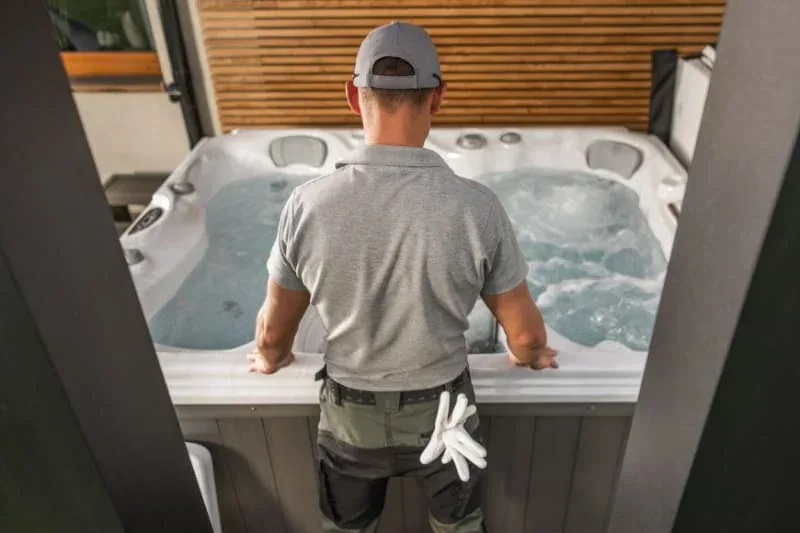 Hot tub service professional inspecting and maintaining spa equipment from behind