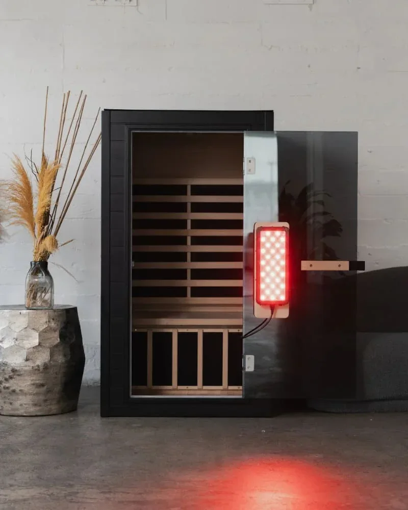 SaunaBox Solara infrared sauna with open glass door and activated red light therapy panel